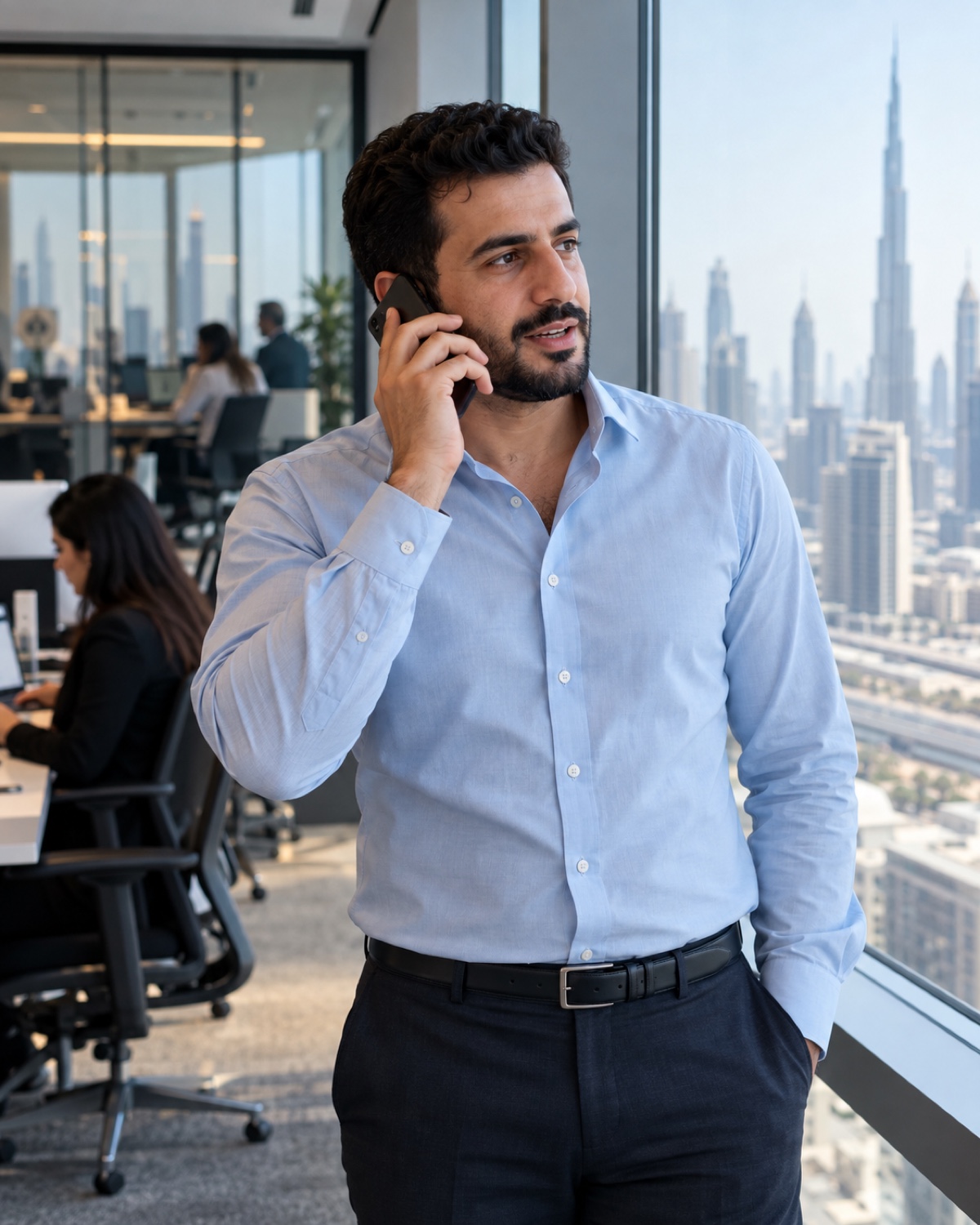 Support engineer in an open-collar shirt taking a phone call by an office window.